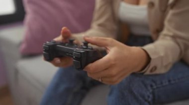 Oturma odasındaki kanepede oturmuş video oyunları oynamaya odaklanan oyun kumandası tutan genç bir kadın..