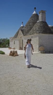 Beyaz elbiseli güzel bir İspanyol kadın güneşli bir günde Puglia, İtalya 'nın tarihi bir kasabası olan Alberobello' daki geleneksel Trulli evlerinin yakınında mutlu bir şekilde yürüyor..