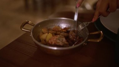 Bir İtalyan restoranında çatal ve bıçak kullanarak ahşap bir masaya yerleştirilmiş metal bir tabakta servis edilen lezzetli bir yemeği yiyen genç bir kadın..