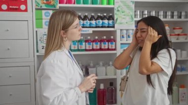 Bir kadın eczacı, ilaç ve sağlık ürünleri raflarıyla çevrili bir eczanede sıkıntılı bir kadın müşteriye tavsiyede bulunuyor..