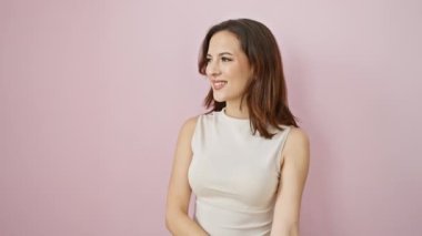 Kolsuz tişört giyen, neşeli bir gülüşle doğal olarak gülümseyen, kenarda duran kendinden emin genç İspanyol kadın. Hepsi izole edilmiş pembe bir arka planda oluyor..