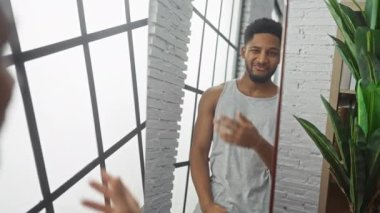 Evdeki aynada yansımasıyla etkileşime geçen neşeli bir Afrikalı Amerikalı adam. Etrafı ev bitkileri ve modern dekorlarla çevrili..