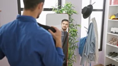 Yakışıklı İspanyol adam gülümsüyor, modern odada elbise askısı ve bitkisi ile takım elbise tutuyor..