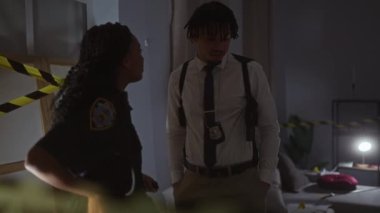 Bir kadın polis memuru ve bir erkek müfettiş kapalı bir yerde ciddi bir şekilde sohbet ediyorlar..