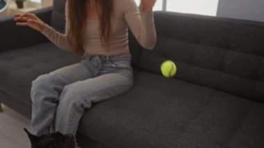 Genç bir kadın sıcak bir oturma odasında kanepede oturup buldoguyla oynarken ellerini çırpıyor..