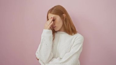 Yorgun kızıl saçlı kadın, stresle boğulmuş acı dolu gözlerini ovalıyor, pembe izole edilmiş arka plana karşı bir kazak giyiyor, yorgunluk ve baş ağrısı portresi çiziyor..