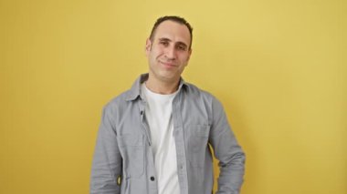 Neşeli genç İspanyol adam, zafer işareti atarak kameraya kendinden emin bir gülümseme sergiliyor. Sarı arka planda izole edilmiş, o olumlu bir galibiyetin timsali..