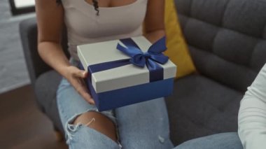 Beyaz gömlekli bir adam salonda bir kadına mavi kurdeleli bir hediye sunuyor. İçerideki sıcak ortamda aşkı ve kutlamaları simgeliyor..