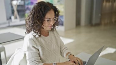 Gözlüklü, kendine güvenen İspanyol kadın modern ofiste dizüstü bilgisayarla çalışıyor..