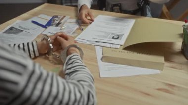 Elleri kelepçeli ve masasında inceleme yapan biri polis karakolunda sorgulandığını öne sürüyor..
