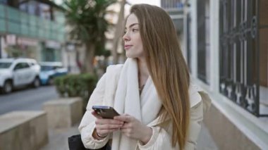 Şehrin işlek bir köşesinde akıllı telefon kullanan genç bir kadın..