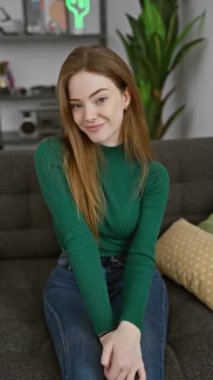 Neşeli genç sarışın kadın iki parmağıyla neşeli bir zafer işareti gösteriyor, evinde kalın bir kazak giyiyor. Kendinden emin bir gülümseme pozitiflik ve başarı yayıyor..