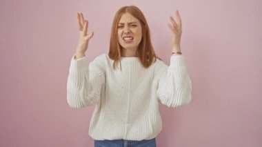 Hırkalı, öfkeli, genç, kızıl saçlı bir kadın öfkesini kanalize ediyor. Pembe bir arka planda izole edilmiş, patlayıcı bir duygu gösterisiyle kollarını kaldırarak çılgınca bağırıyor..