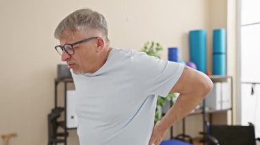 Gözlüklü, klinik ortamında sırt ağrısı çeken olgun bir adam. Sağlık ve üst düzey sorunların göstergesi..