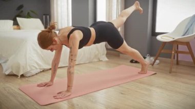 Formda bir kadın modern bir yatak odasında pembe bir yoga minderinin üzerinde tahtayla egzersiz yapıyor ve sağlıklı bir yaşam tarzı sergiliyor..