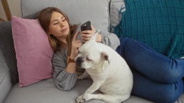 Genç bir kadın ve köpeği oturma odasında birlikte rahatlarken, kadın evin içinde bir kanepede uzanmış telefonuna göz gezdiriyordu..