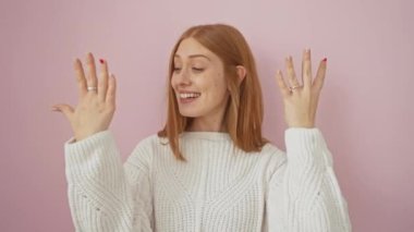 Neşeli, genç, kızıl saçlı, süveter giyen, kendine güvenen, parmaklarını pembe izole arka planda gezdiren bir kadın.