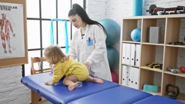 Rehabilitasyon kliniğindeki küçük kızı fizyoterapi ekipmanlarıyla değerlendiren bir kadın doktor.