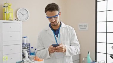 Laboratuvar ortamında akıllı telefon kullanan İspanyol erkek bilim adamı modern sağlık teknolojisi entegrasyonunu aktarıyor..