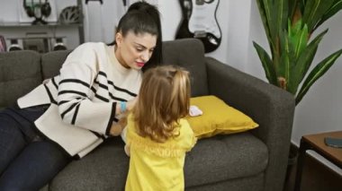 Gülümseyen bir kadın ve küçük kızı güzel dekore edilmiş bir oturma odasında rahat bir kanepede birlikte iyi vakit geçiriyorlar..