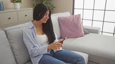 Uzun esmer saçlı, Latin kökenli genç bir kadın evinde oturmuş, akıllı telefonuyla konuşuyor..