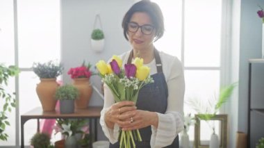 Gülümseyen orta yaşlı bir kadın. Parlak, kapalı bir çiçekçide laleler düzenliyor..