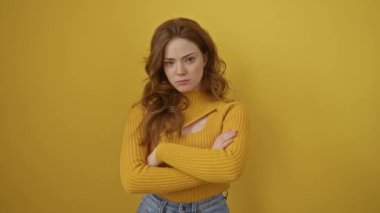 Süveter giyen, kuşkucu ve gergin genç beyaz bir kadın yüzünde çapraz kollu tasvip etmeyen bir ifade var. Negatif. izole edilmiş sarı arkaplan