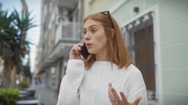 Şehir caddesinde telefonda konuşan, süveter giymiş endişeli genç bir kadın.