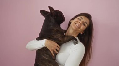 Genç bir İspanyol kadın, izole edilmiş pembe bir arka plana karşı bir buldog tutuyor, neşe ve sıcaklık saçıyor..