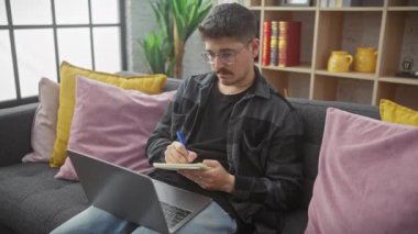 Düşünceli bir adam, iyi ışıklandırılmış oturma odasında rahat koltuğunda çalışırken not defterine not alır..