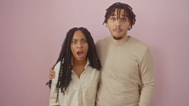 Göz kamaştırıcı bir çift, inançsızlıktan ağzı açık, izole edilmiş pembe bir arkaplanda şaşkın şaşkın duruyorlar, yüzleri bir şok ve heyecan karışımı.