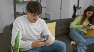 Bir erkek ve bir kadın, modern bir oturma odasındaki akıllı telefonları kullanarak ayrı ayrı bir koltukta oturur ve bağlantısızlık tasvir ederler..