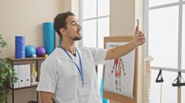 Klinikteki genç İspanyol bir adam akıllı telefonuyla özçekim yapıyor. Profesyonel ama sıradan bir tavır sergiliyor..