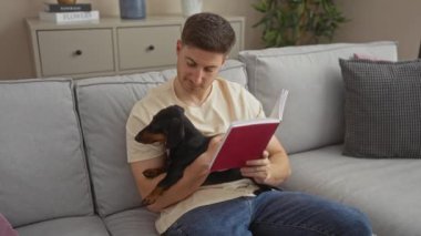 Genç İspanyol bir adam, tekelini sıcak bir oturma odasında tutarken kitap okuyor ve evcil bir hayvanla rahat bir ev ortamını gösteriyor..