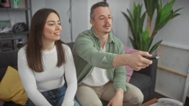 Bir kadın ve bir erkek, sıcak bir oturma odasında, uzaktan kumandayı kullanırken gülümsüyorlar..