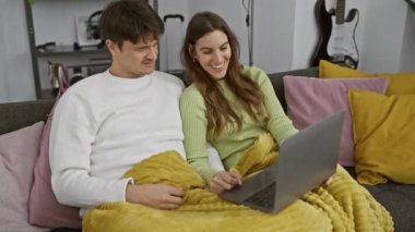 Çift evlerinde rahat bir oturma odasında dizüstü bilgisayarla vakit geçiriyorlar. Teknoloji, eğlence ve ilişki sergiliyorlar..