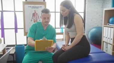 Fizyoterapist, rehabilitasyon odasında kadın hastayla konuşurken not alıyor..