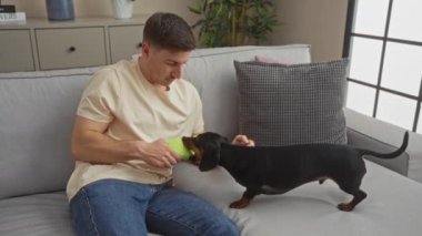 Genç İspanyol bir adam, rahat bir oturma odasında köpeğiyle oynuyor, rahat ve rahat bir ev dekorasyonu sergiliyor..