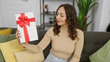 Işıl ışıl genç Afrikalı Amerikalı kadın, 'tamam' tabelasıyla sevinç ve onayı ifade ediyor, doğum günü hediyesini tutuyor, oturma odasında pozitif enerjiyle ışıldıyor..