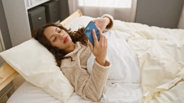 Yatak odasında akıllı telefon kullanan genç bir kadın rahat bir evde rahatlama ve teknoloji tasvir ediyor.