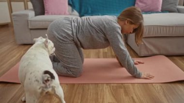 Oturma odasındaki minderde yoga yapan genç bir kadın yanında köpek evcil hayvanıyla ev ortamını sergiliyor..