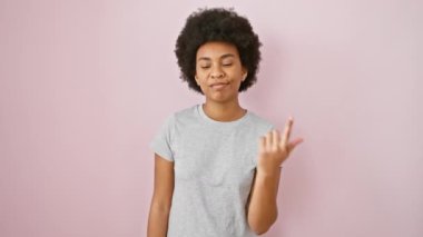 Neşeli Afro-Amerikalı kadın gururla parmak kaldırıyor, pembe bir arka planda duruyor, günlük bir tişört giyiyor, gülümsüyor ve güzel titreşimler veriyor..