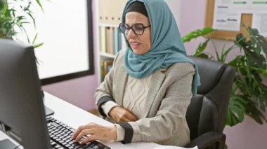 Orta yaşlı İspanyol kadın tesettürlü modern ofiste bilgisayar başında çalışıyor.