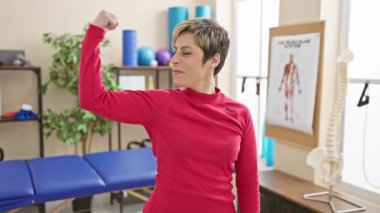 Rehabilitasyon merkezinde güç gösterisi yapan gülümseyen bir kadın.