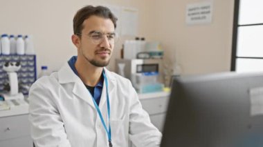 Laboratuvar önlüklü genç bir İspanyol modern bir laboratuvar ya da klinik ortamında bilgisayar başında çalışıyor..