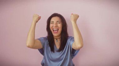 Heyecanlı orta yaşlı İspanyol kadın zaferini kutlarken sevinçten deliye dönüyor! Kollarını kaldırmış, yüzünde çılgın bir başarıyla, izole edilmiş pembe bir arka plana karşı duruyormuş..