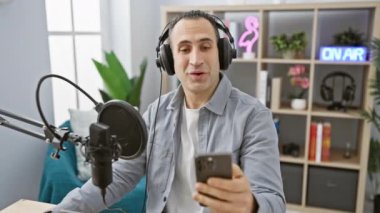 Radyoda kulaklık takmış gülümseyen İspanyol bir adam akıllı telefon ve mikrofonla iletişim kuruyor..