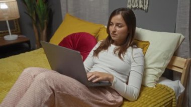 Genç bir kadın dizüstü bilgisayarını kapatıp yumuşak yastıklar ve sıcak aydınlatmalarla dekore edilmiş rahat bir yatak odasında yatar..