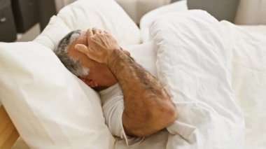 Olgun bir erkek yatakta dinlenir. Yatak odası ortamında rahatlama ya da yorgunluk hissi taşır..