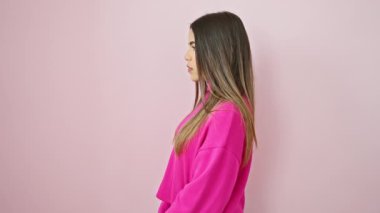 Genç Latin kadının yüzünde kendine güvenen bir gülümseme parıldıyor, sıradan bir poz veriyor, pembe arka planda bir süveter sallıyor - doğal güzellik yan yana